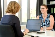 Person an Notebook an einem Schreibtisch, Frau sitzt gegenüber. 